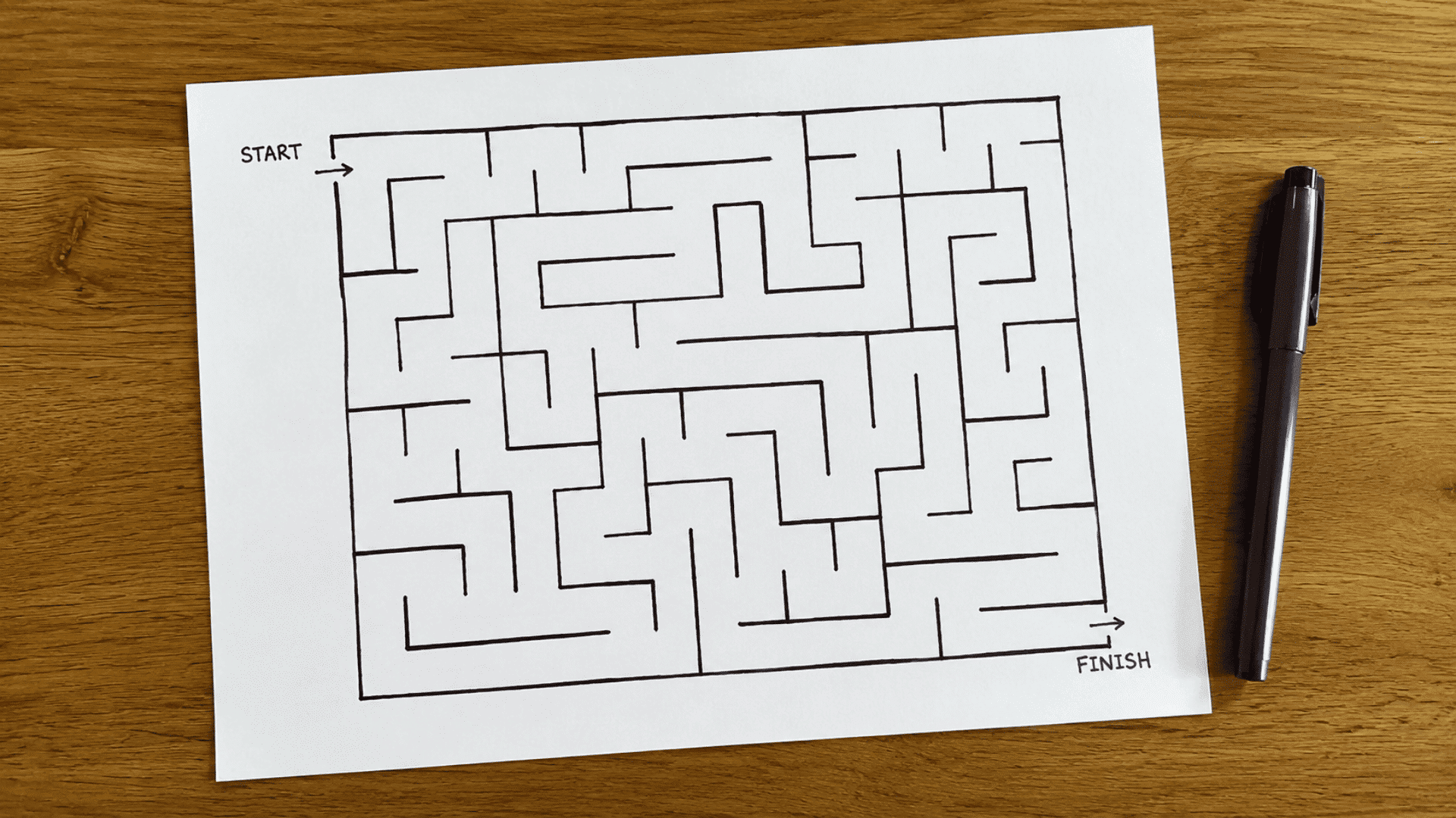 pen and paper game setup on a rustic brown wooden table with hand drawn maze black sketch pen on side and start and end markings (1)
