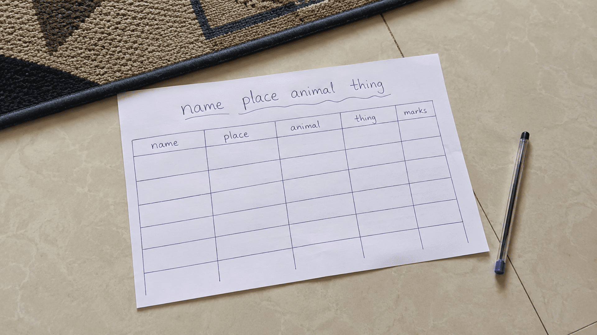 pen and paper games setup with handwritten name place animal thing game setup on tiled floor with pen and white paper mat corner visible on side