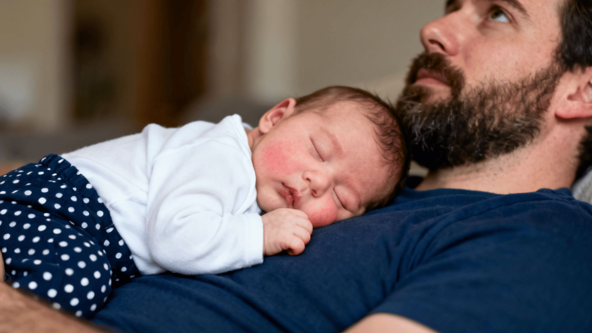 sleeping newborn resting on a parent’s chest with rosy cheeks and a peaceful expression in a warm home setting