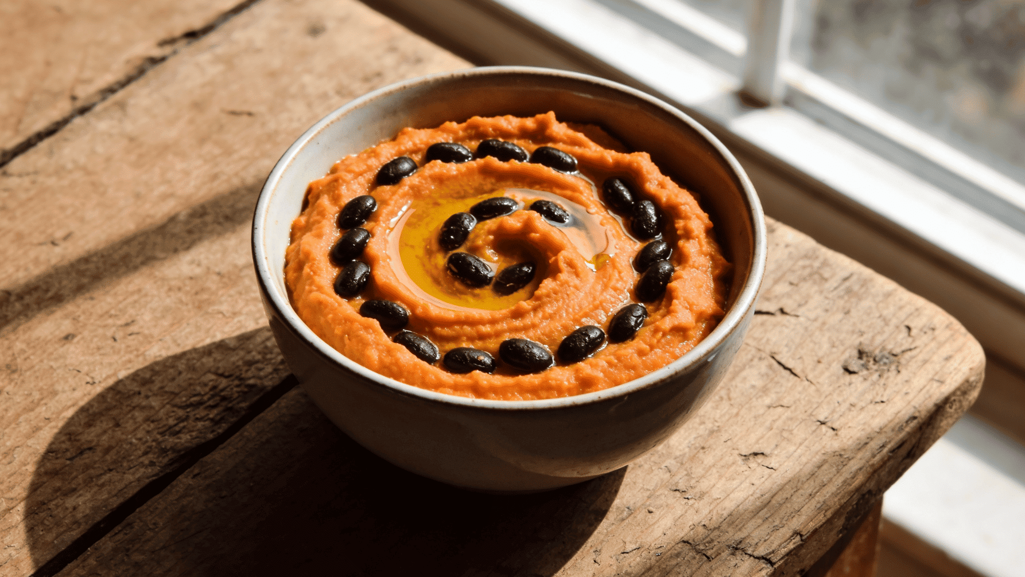 smooth orange sweet potato mash with black beans and a knob of butter in a white bowl