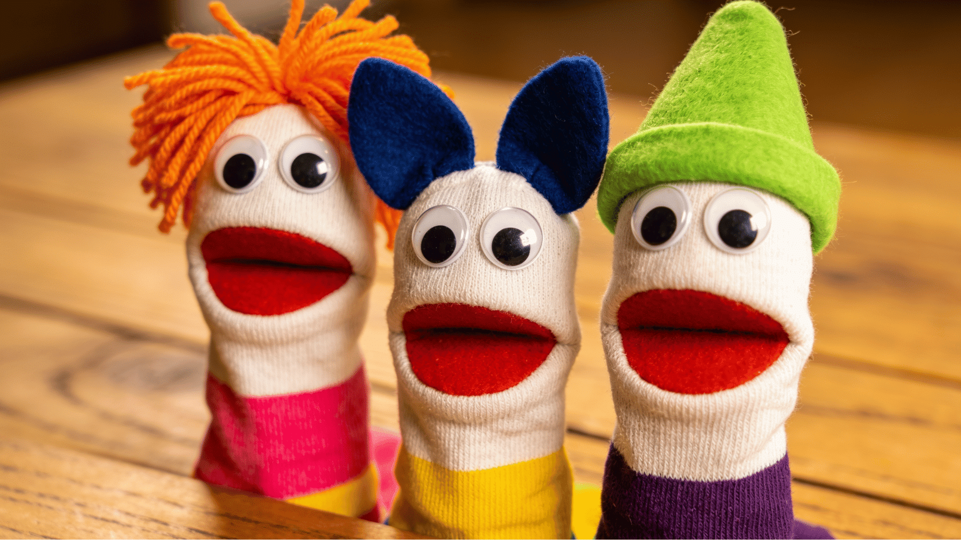 three colorful sock puppets with yarn hair felt accessories and googly eyes propped on a wooden surface