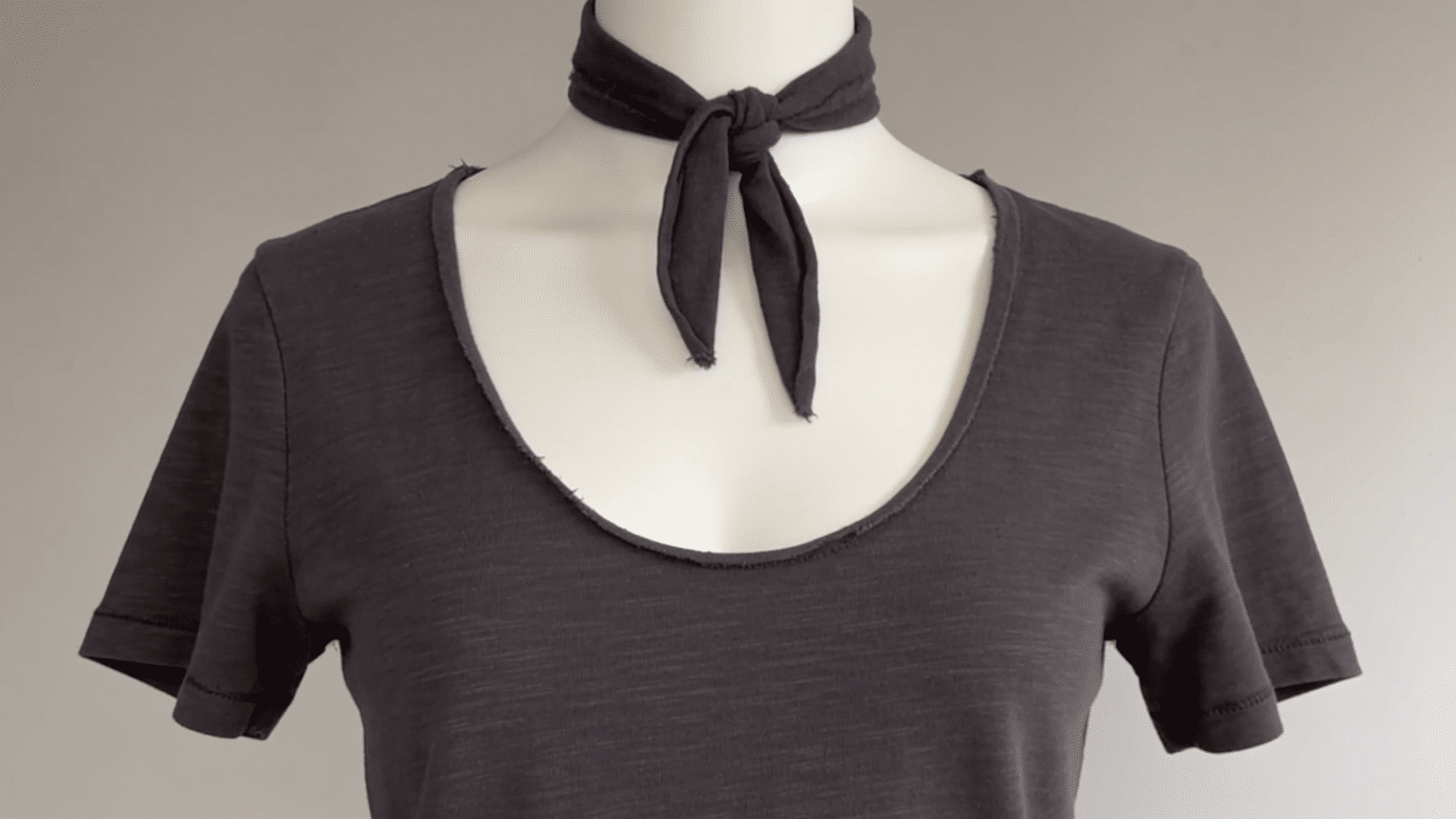 Charcoal t-shirt with a deep scoop neckline and the removed collar strip knotted at the center as a choker detail, mannequin torso shot,