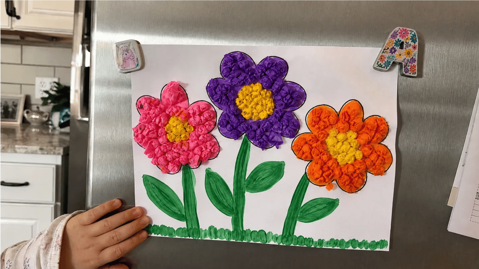 child's tissue paper flower craft with pink, purple and orange flowers displayed on a fridge