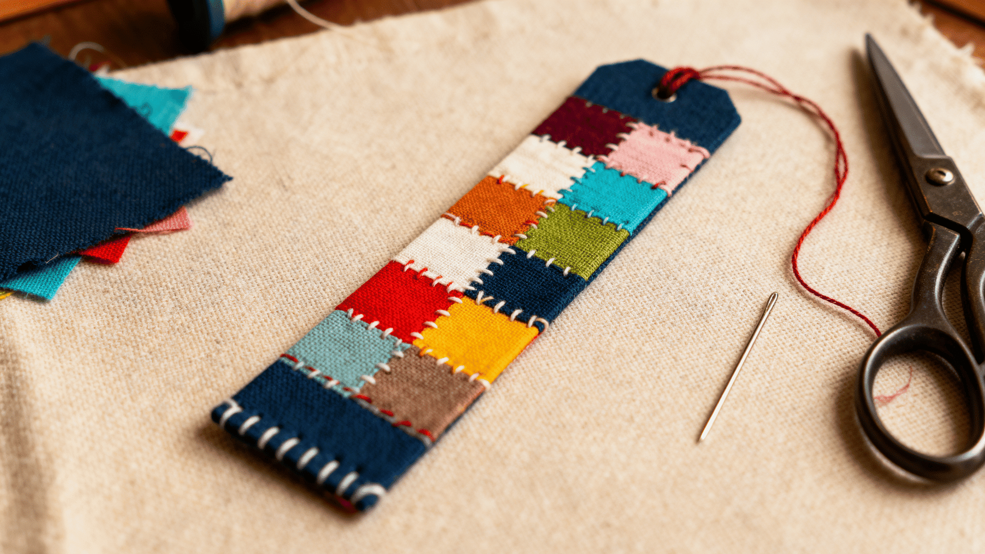 colorful fabric patchwork bookmark with stitched patterns made from fabric pieces displayed with sewing supplies on table