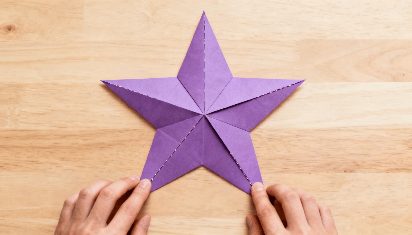 completed purple five-point paper star on a wooden table, with hands making final alignment adjustments to the finished design
