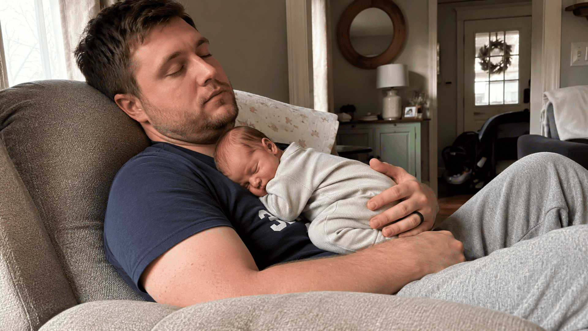 father napping in armchair with sleeping newborn on his chest, cozy home living room, soft natural light