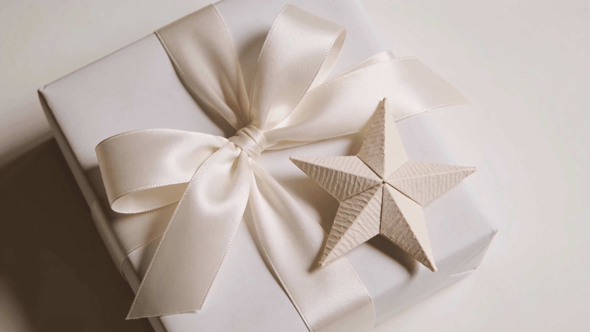 gift box wrapped in white paper with a satin ribbon bow and a handmade paper star attached as a decorative accent
