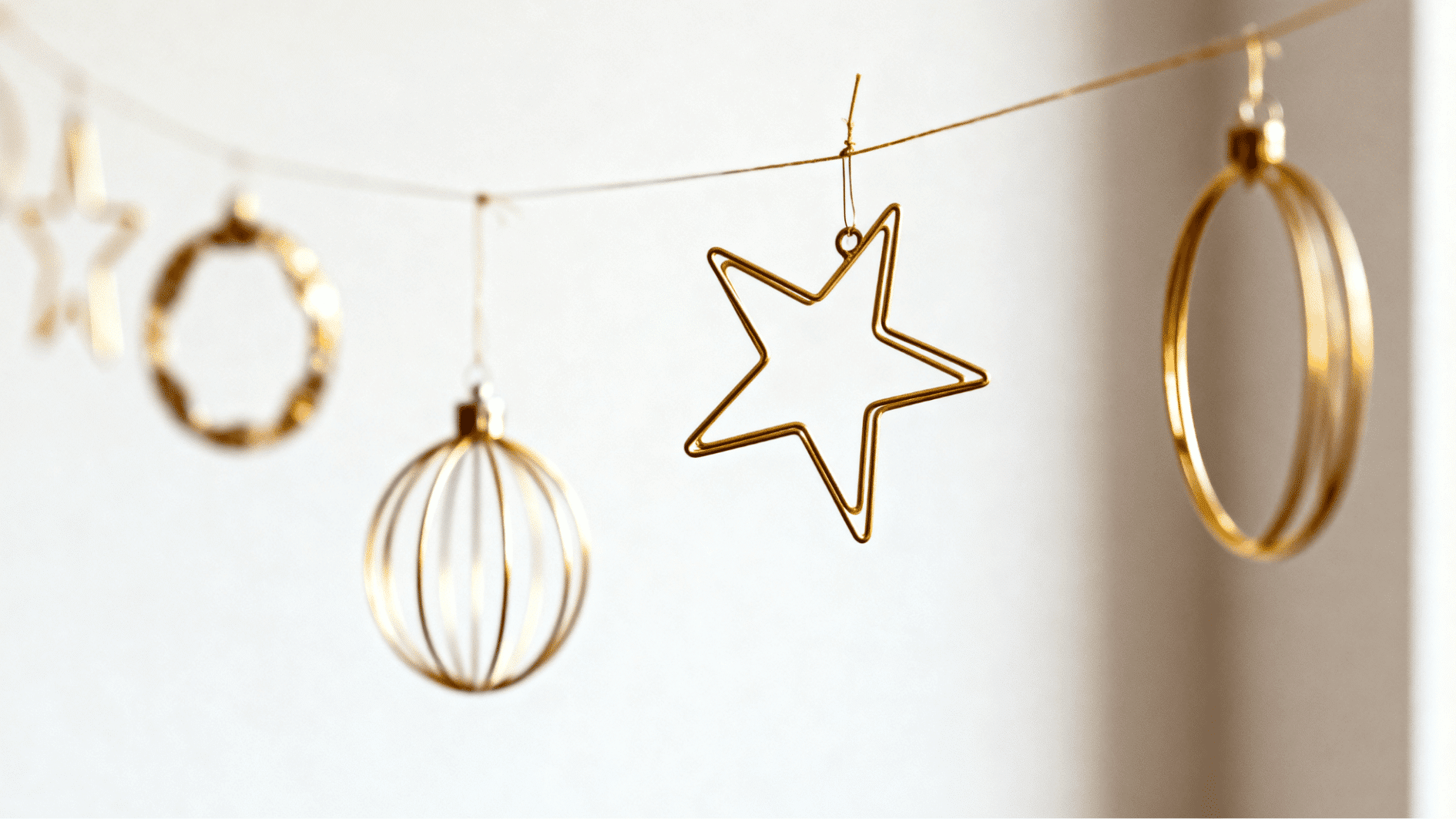 gold wire star ornament hanging on string with minimalist geometric baubles in warm neutral tones against soft blurred background
