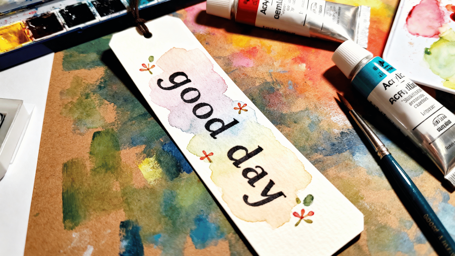 hand painted quote bookmark with colorful background and lettering design displayed with brushes and painting supplies