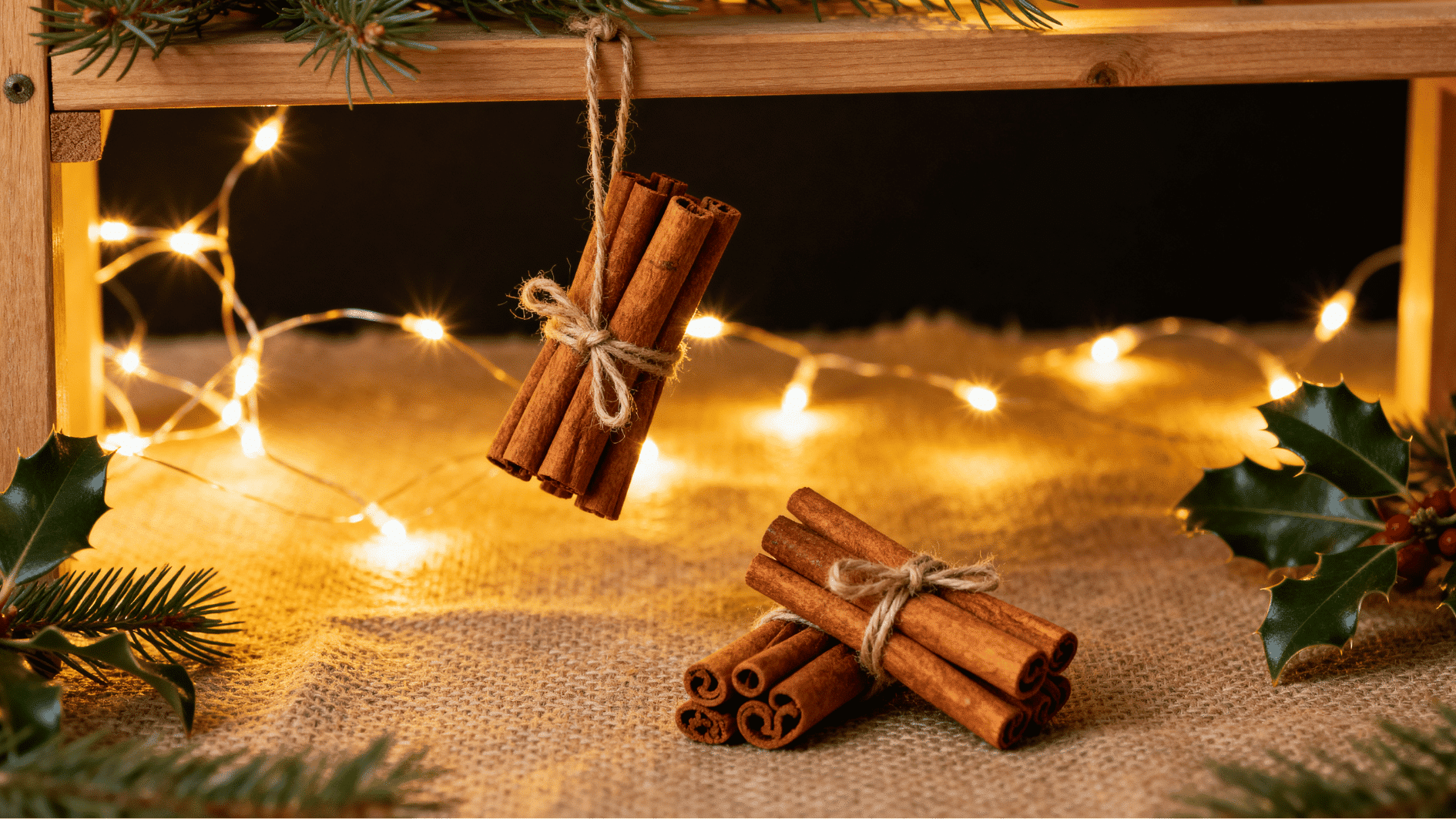 handmade cinnamon stick bundle ornaments tied with twine hanging under wooden shelf with warm fairy lights rustic christmas decor