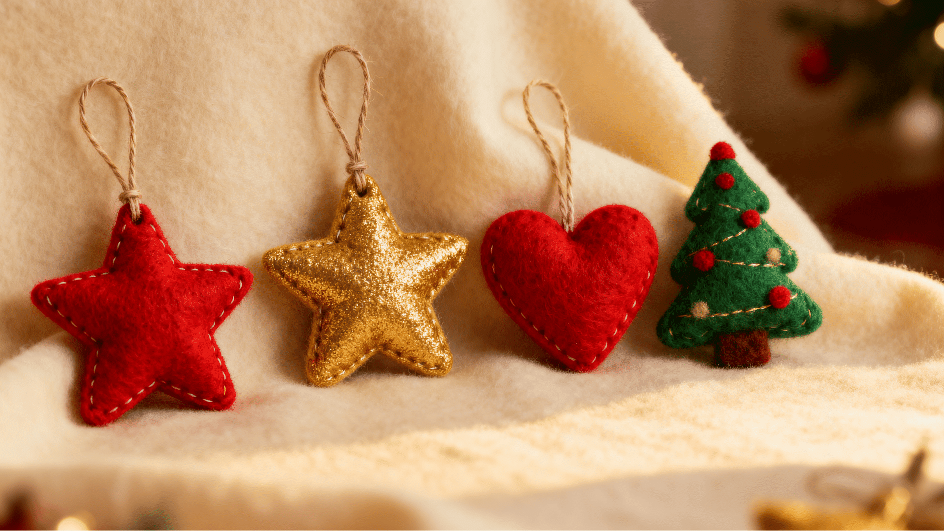 handmade felt christmas ornaments including red star gold star heart and small green tree hanging on fabric with festive lights