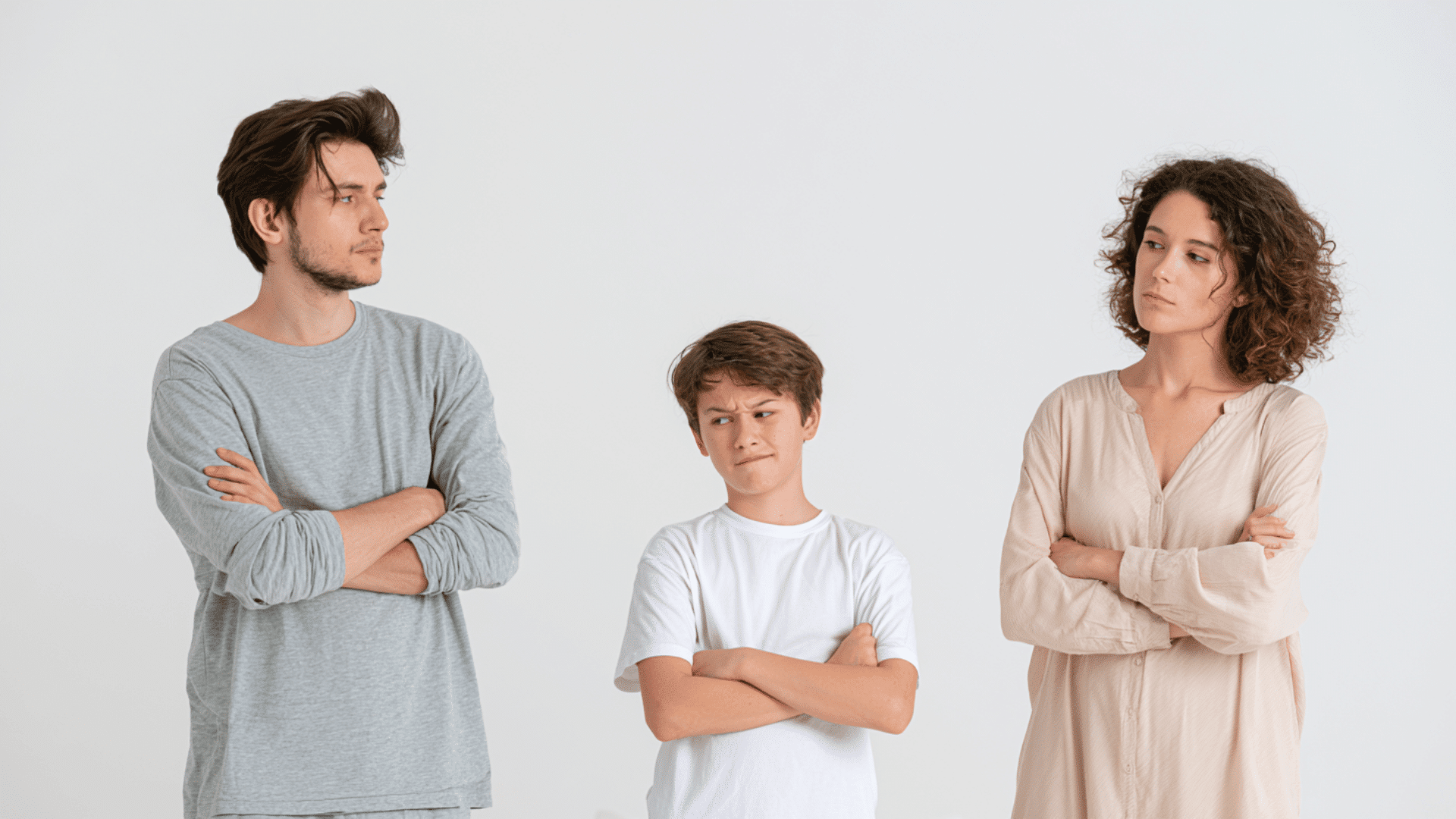 image of left a father a son in middle and mother on right both parents looking towards child with tired pose with tired expression while child is standing hands folded with smirk expressions