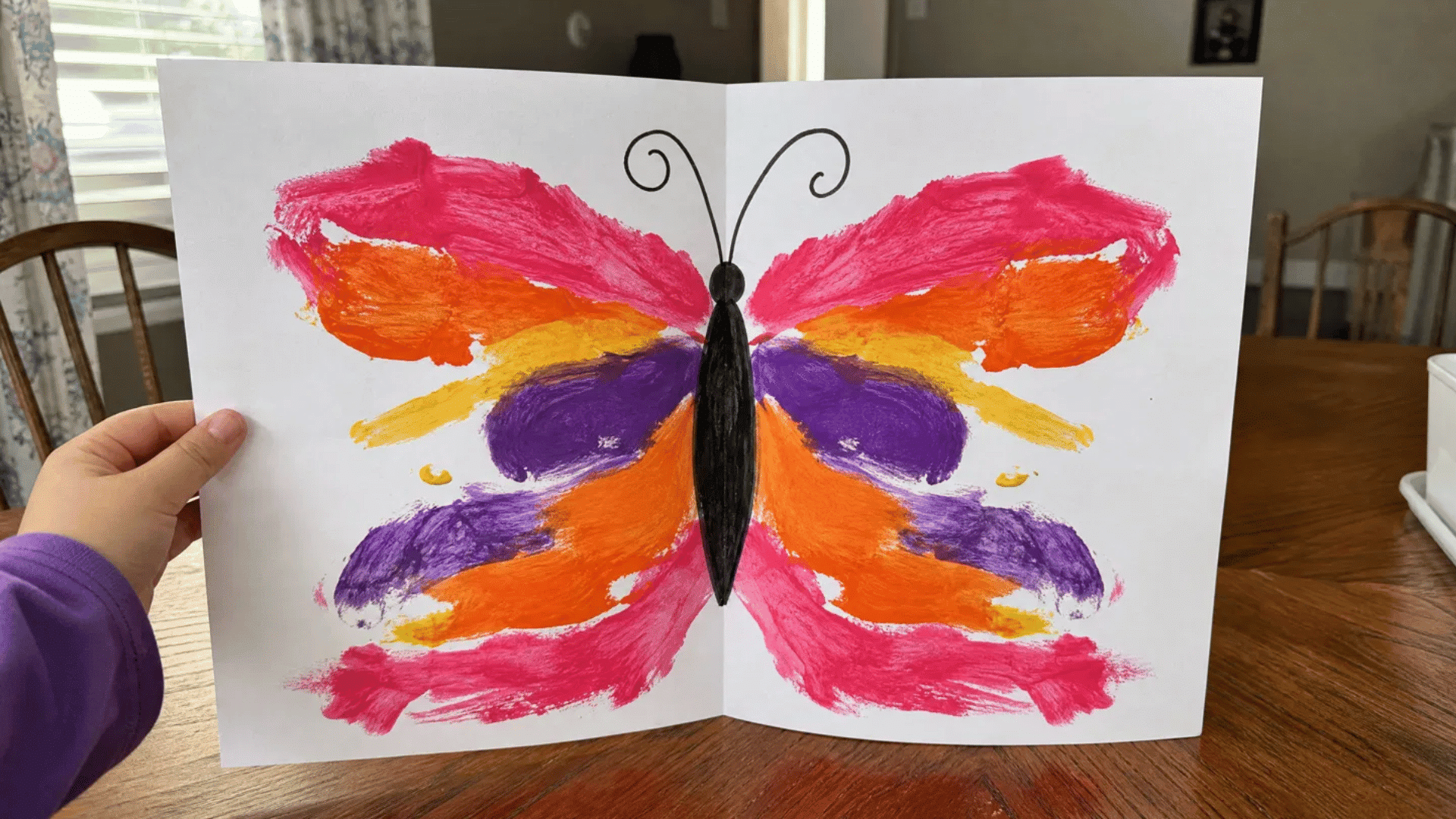 kids butterfly symmetry painting with colorful mirrored wings held open showing fold line in american home