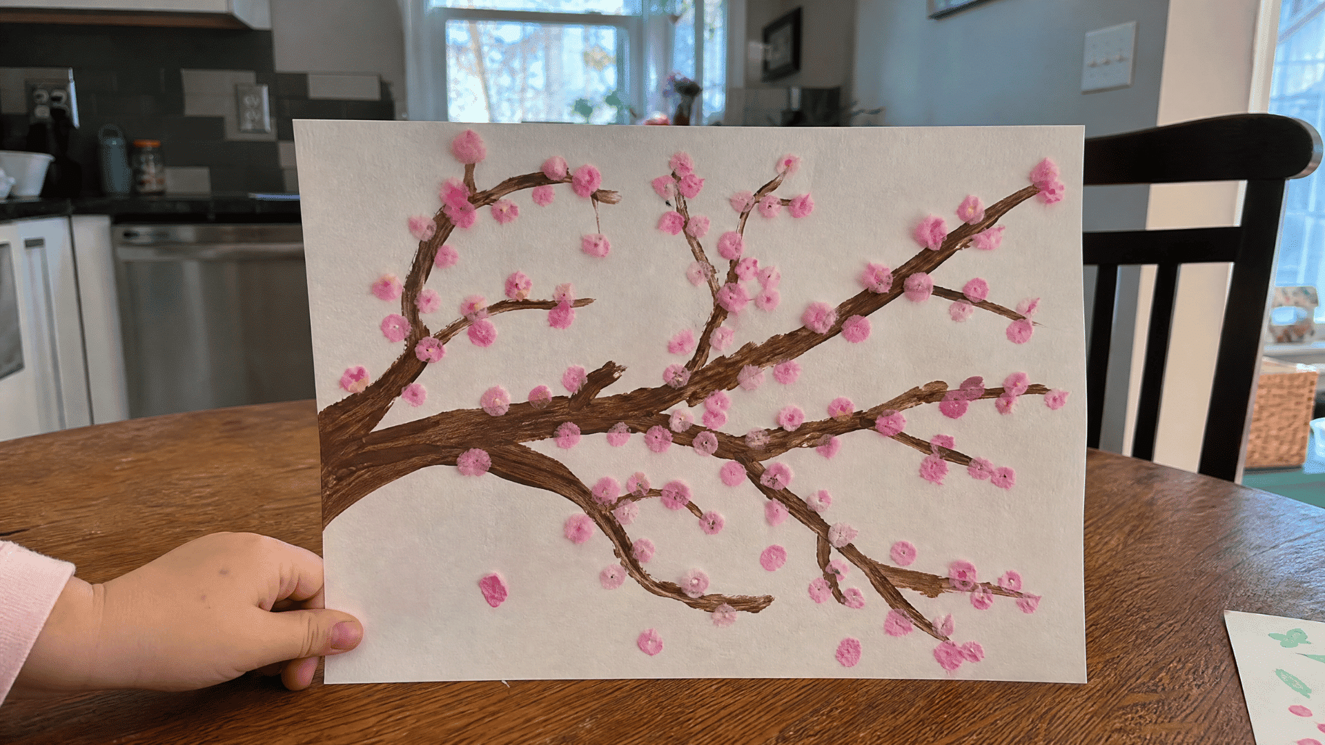 kids cherry blossom tree painting with pink cotton swab blossoms on wooden table in american home kitchen