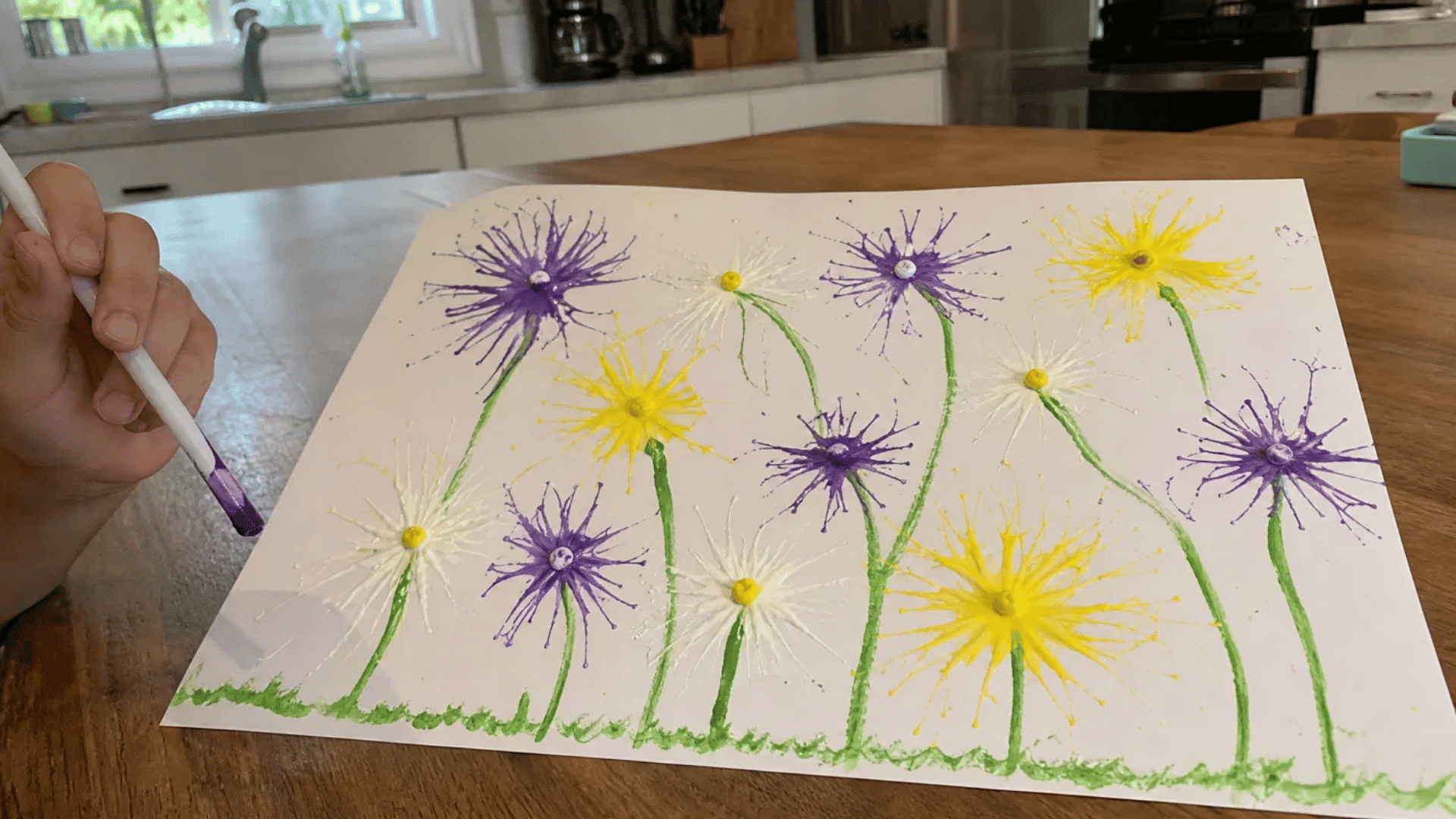 kids dandelion blow painting with purple and yellow straw blown flowers on kitchen table in american home