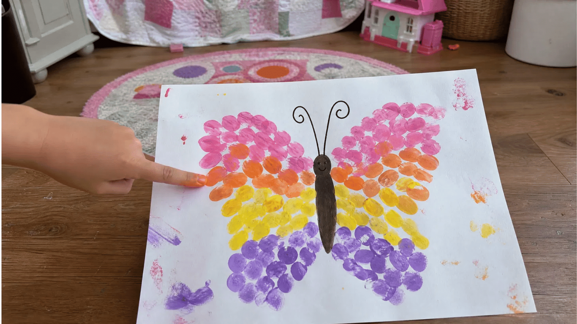 kids fingerprint butterfly art with rainbow colored finger stamp wings on wooden floor in girls bedroom