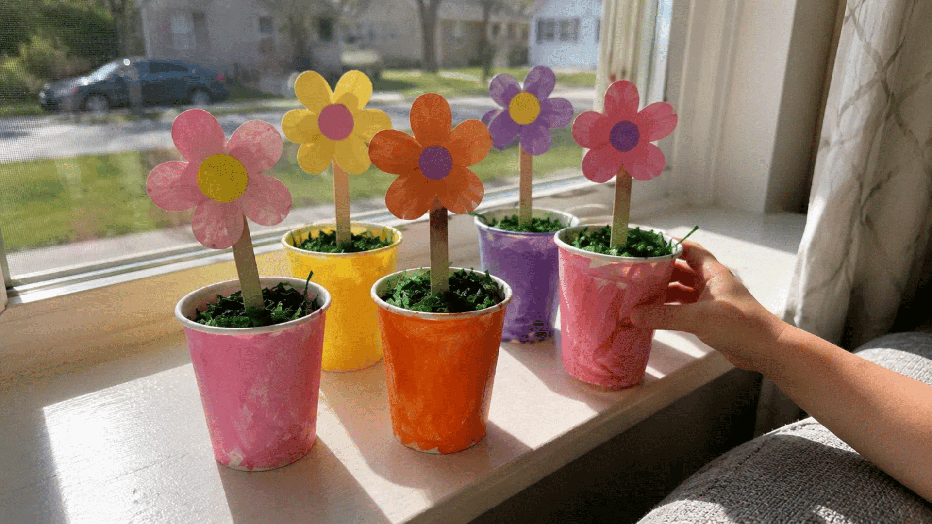 kids paper cup flower garden with colorful painted cups and paper flowers on craft sticks on sunny windowsill