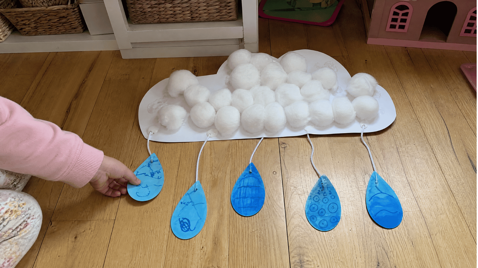 kids rain cloud craft with cotton balls and blue paper raindrops on string on playroom floor
