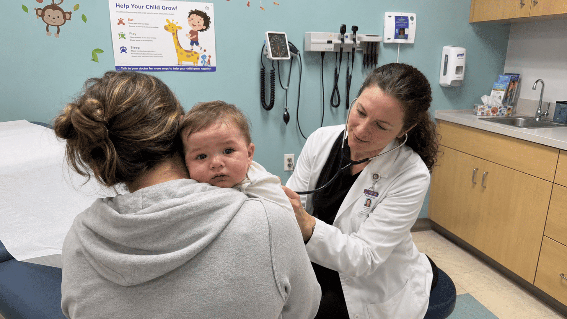 mother holding her sick baby while a pediatrician examines the child with a stethoscope in a clinic