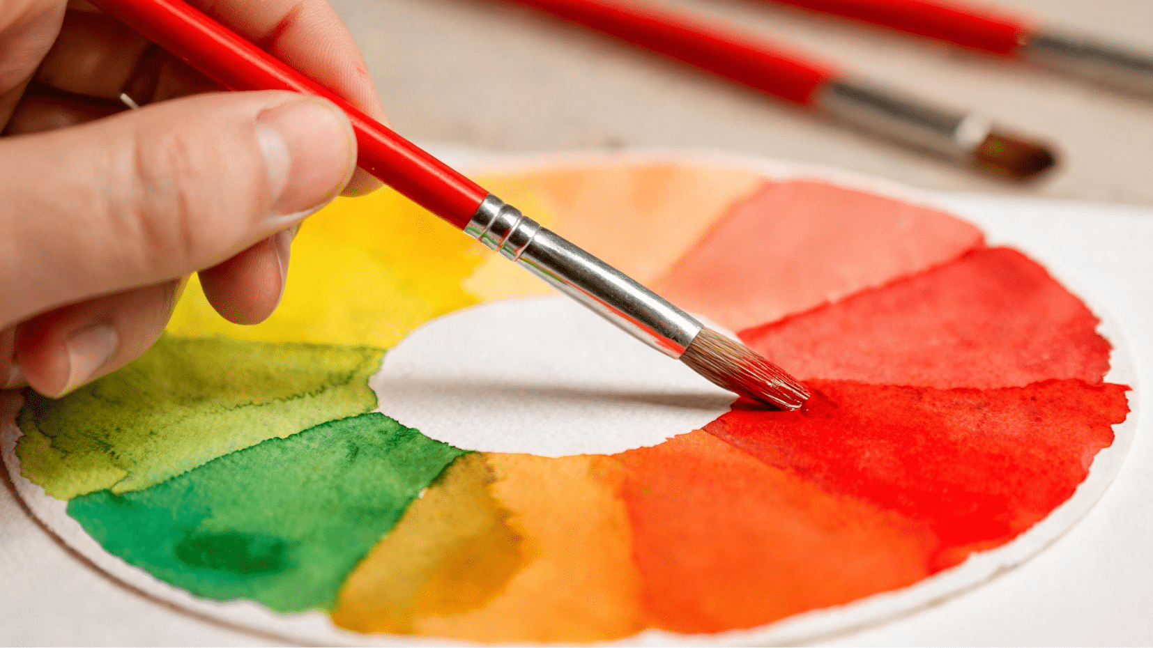 paintbrush applying red watercolor on a color wheel showing color theory practice for artists