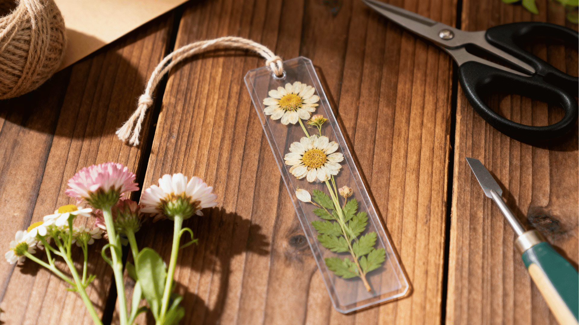pressed flower bookmark with dried flowers and leaves sealed inside a clear layer placed beside natural craft materials