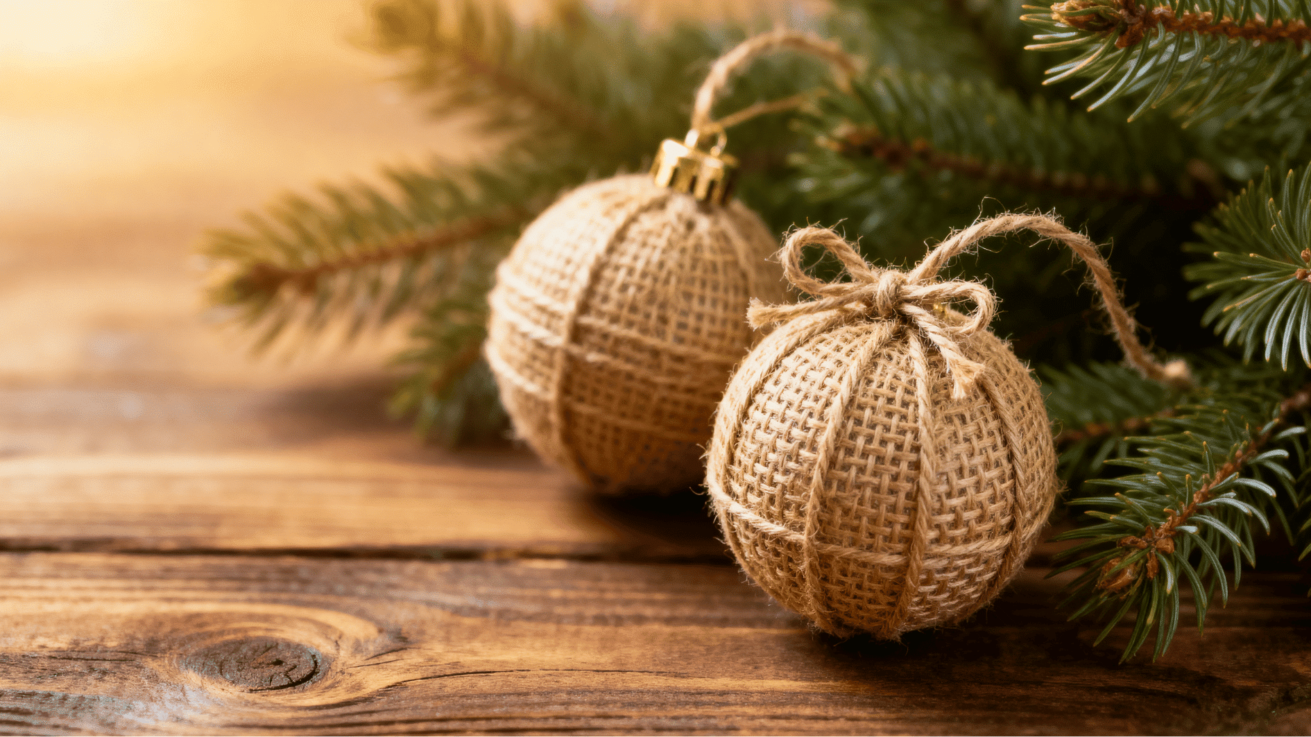 rustic burlap wrapped christmas ornaments tied with twine hanging on wooden branch beside evergreen pine for natural holiday decor