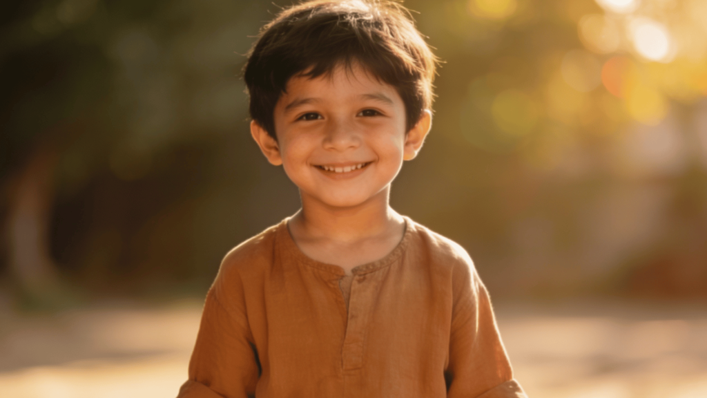 smiling young boy in a brown linen outfit standing outdoors in warm golden sunlight with a soft blurred background