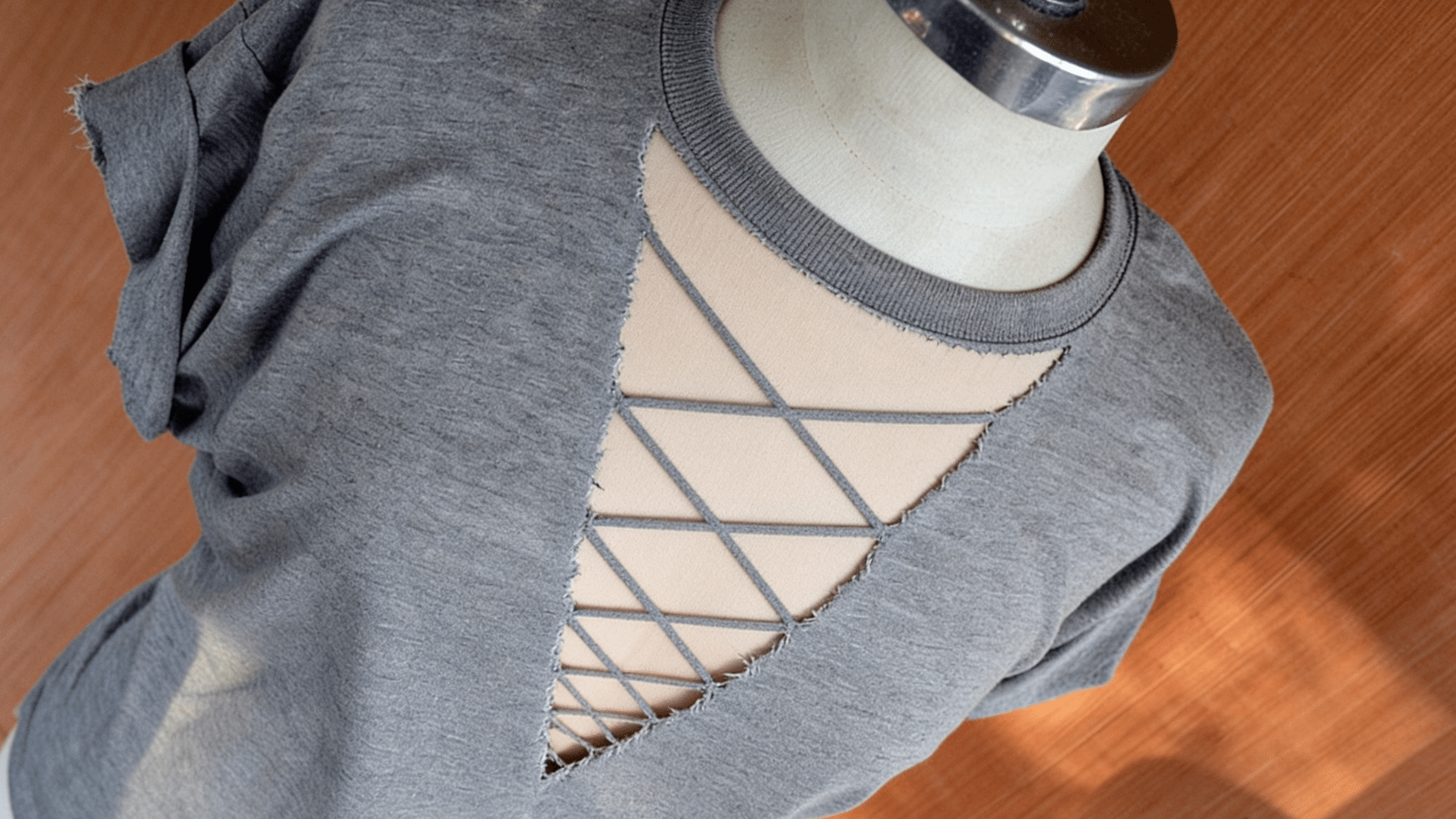 thin strips of the shirt's own jersey crossing diagonally to form diamond-shaped openings that shrink toward the bottom, raw scissor-cut edges slightly curled, skin-tone fabric visible through the