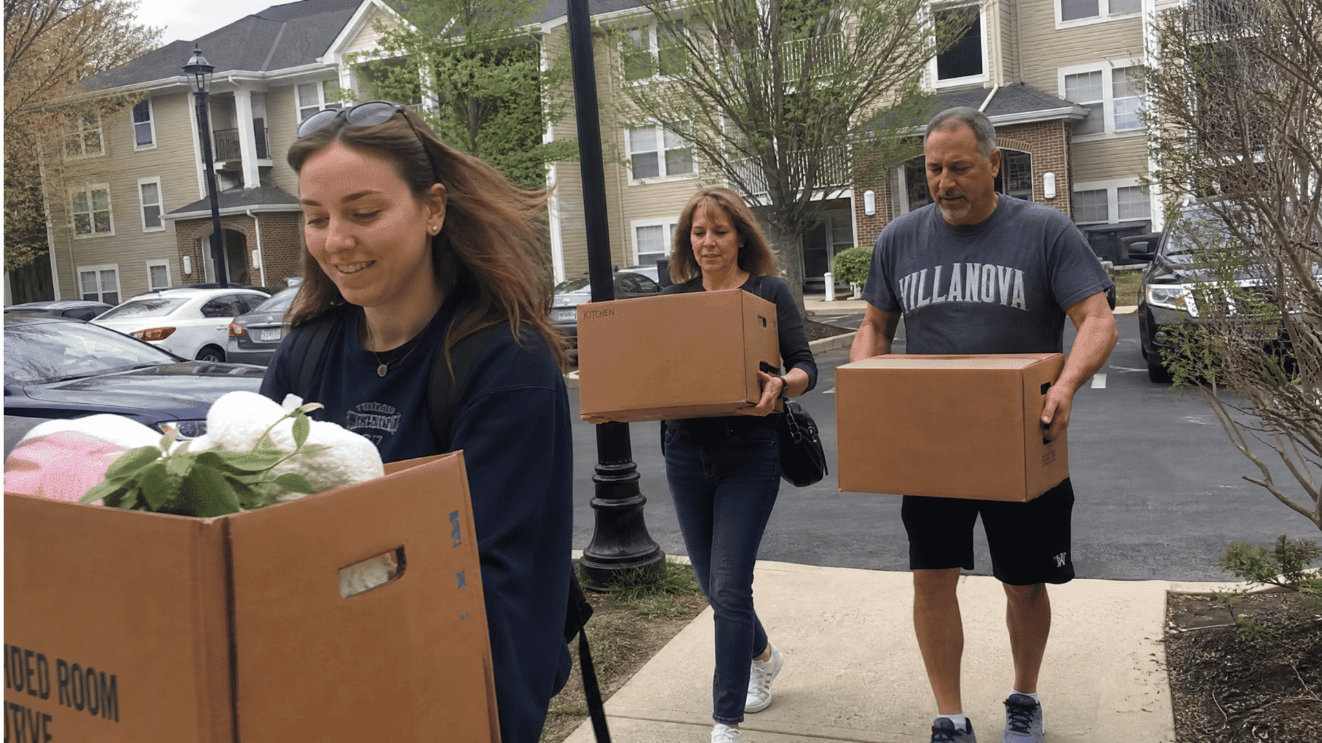 young adults and parents carrying moving boxes outside an apartment building during move out day