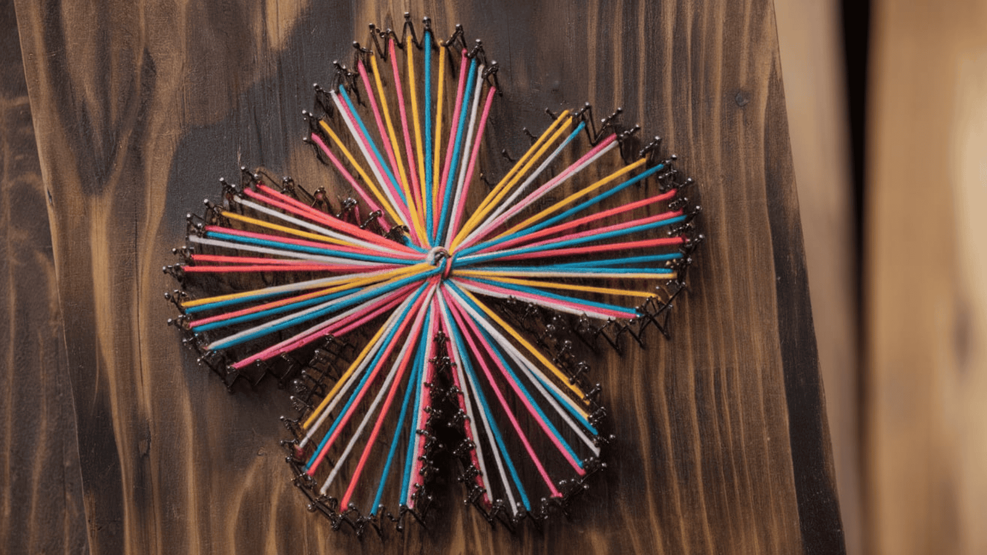 a colorful starburst string art design made with multicolored thread and nails on a dark wood board