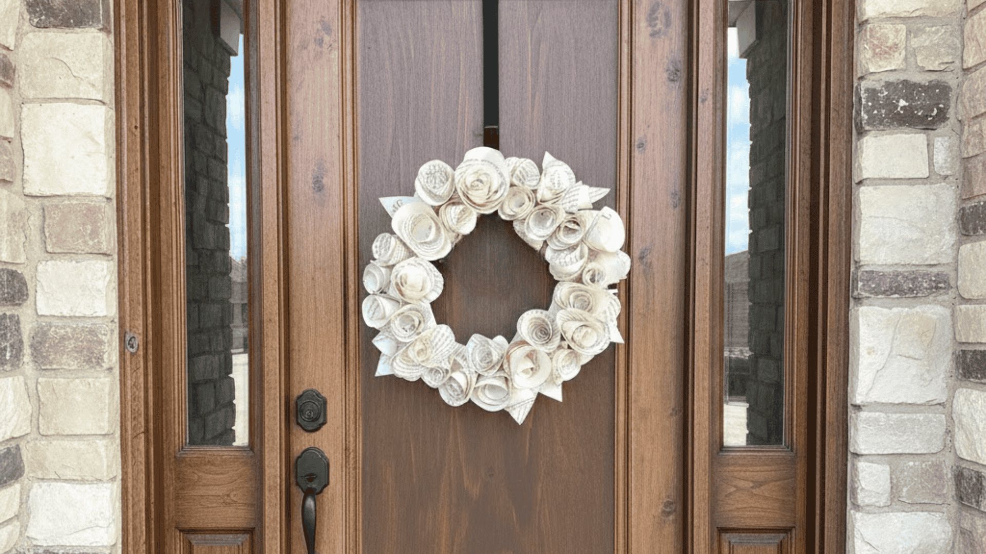 a diy wreath made from rolled book page roses hanging on a wooden front door with stone surrounds