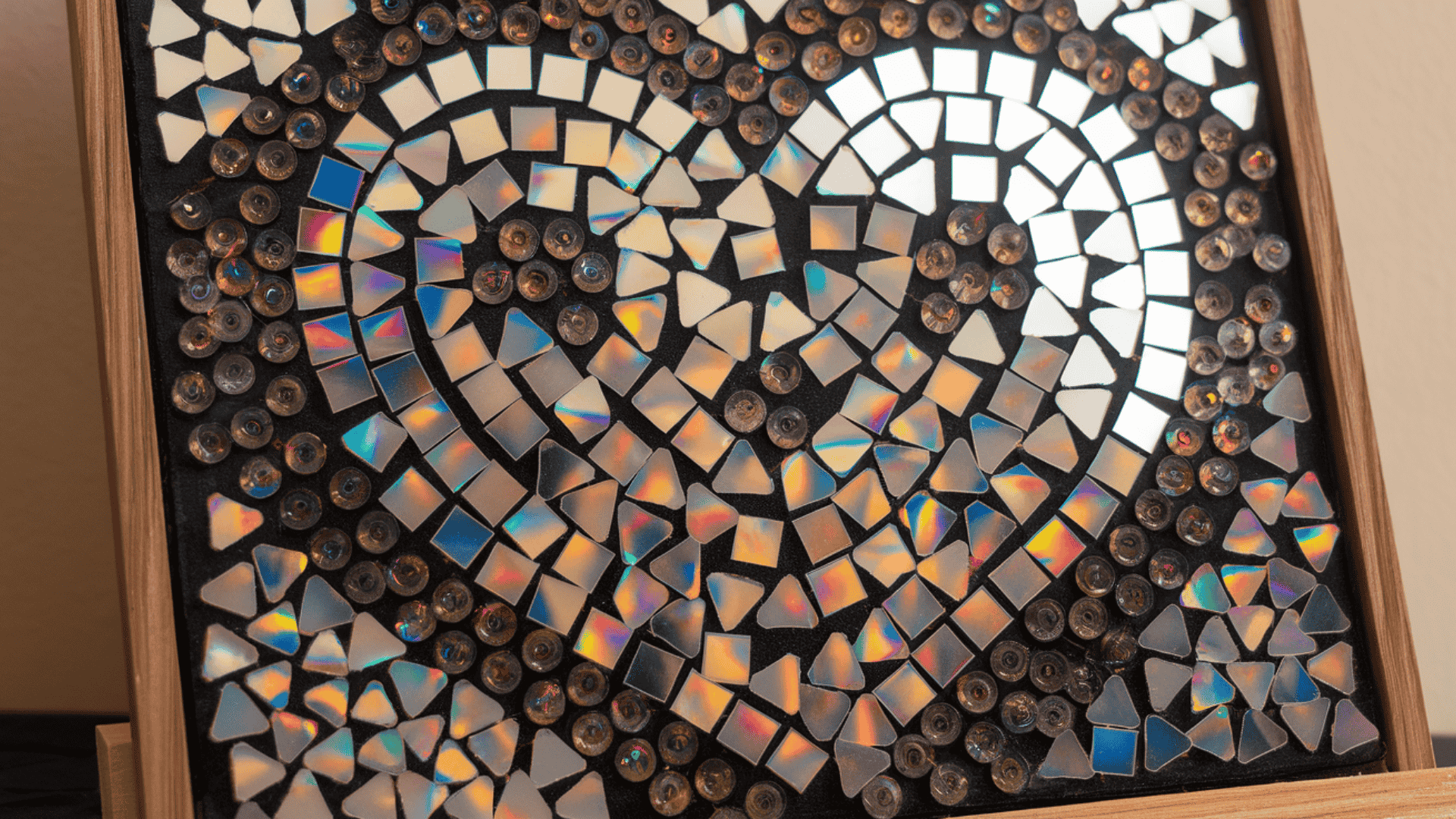 a framed mosaic wall art made from iridescent cd pieces and glass beads in swirling patterns on black
