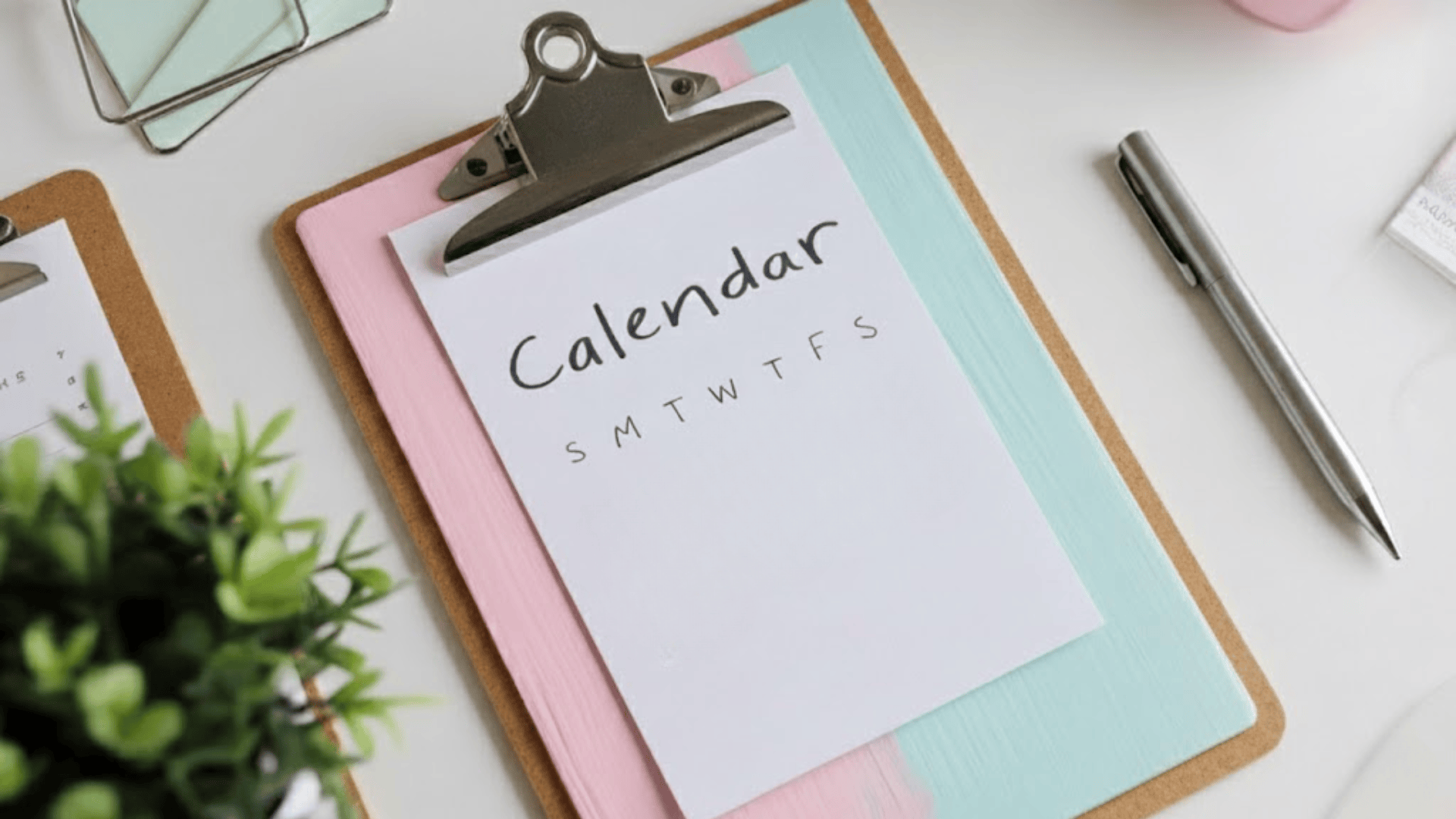 a handmade diy calendar page clipped to a pastel pink and mint painted clipboard on a white desk