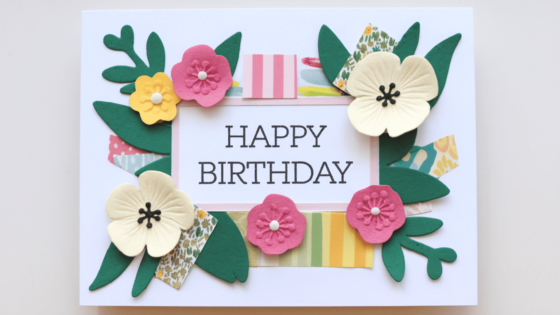 a handmade happy birthday card decorated with paper flowers, green leaves and colorful washi tape borders
