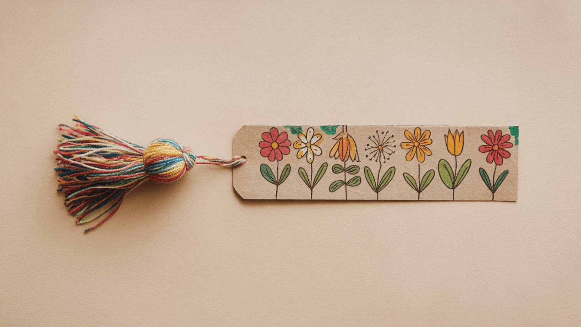 a handmade kraft paper bookmark with hand drawn colorful flowers and a multicolored yarn tassel attached