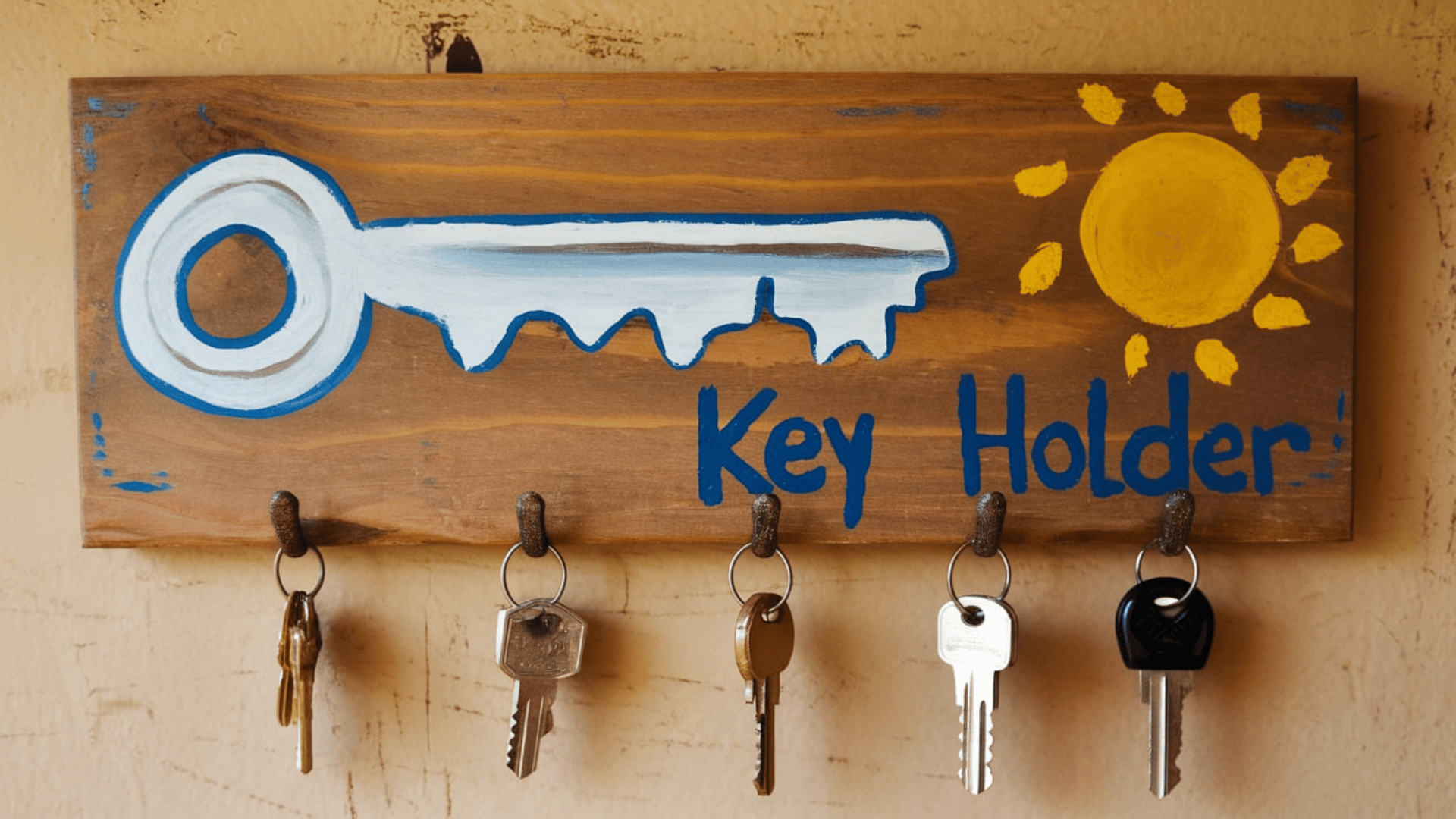 a painted wooden key holder board with blue key and sun design and five metal hooks holding keys
