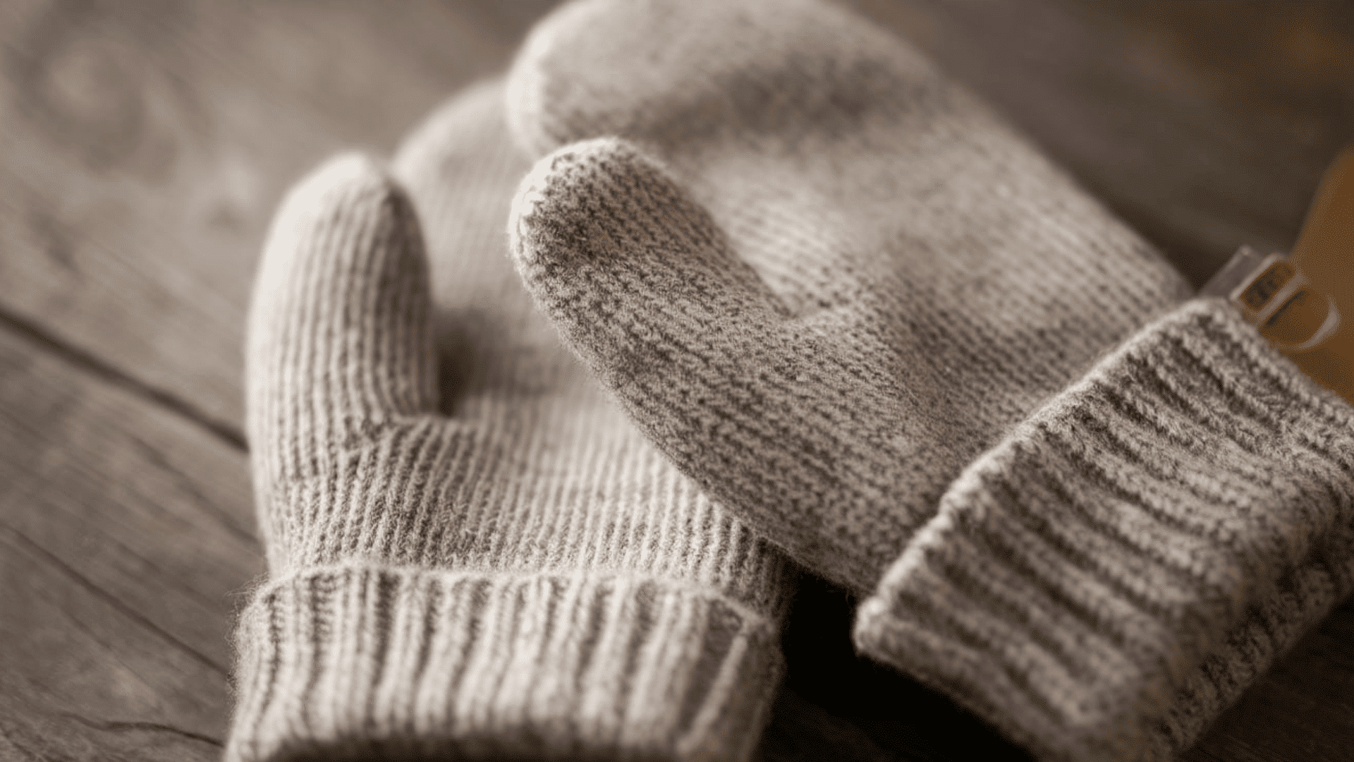 a pair of soft gray handknitted wool mittens with ribbed cuffs placed on a rustic wooden surface