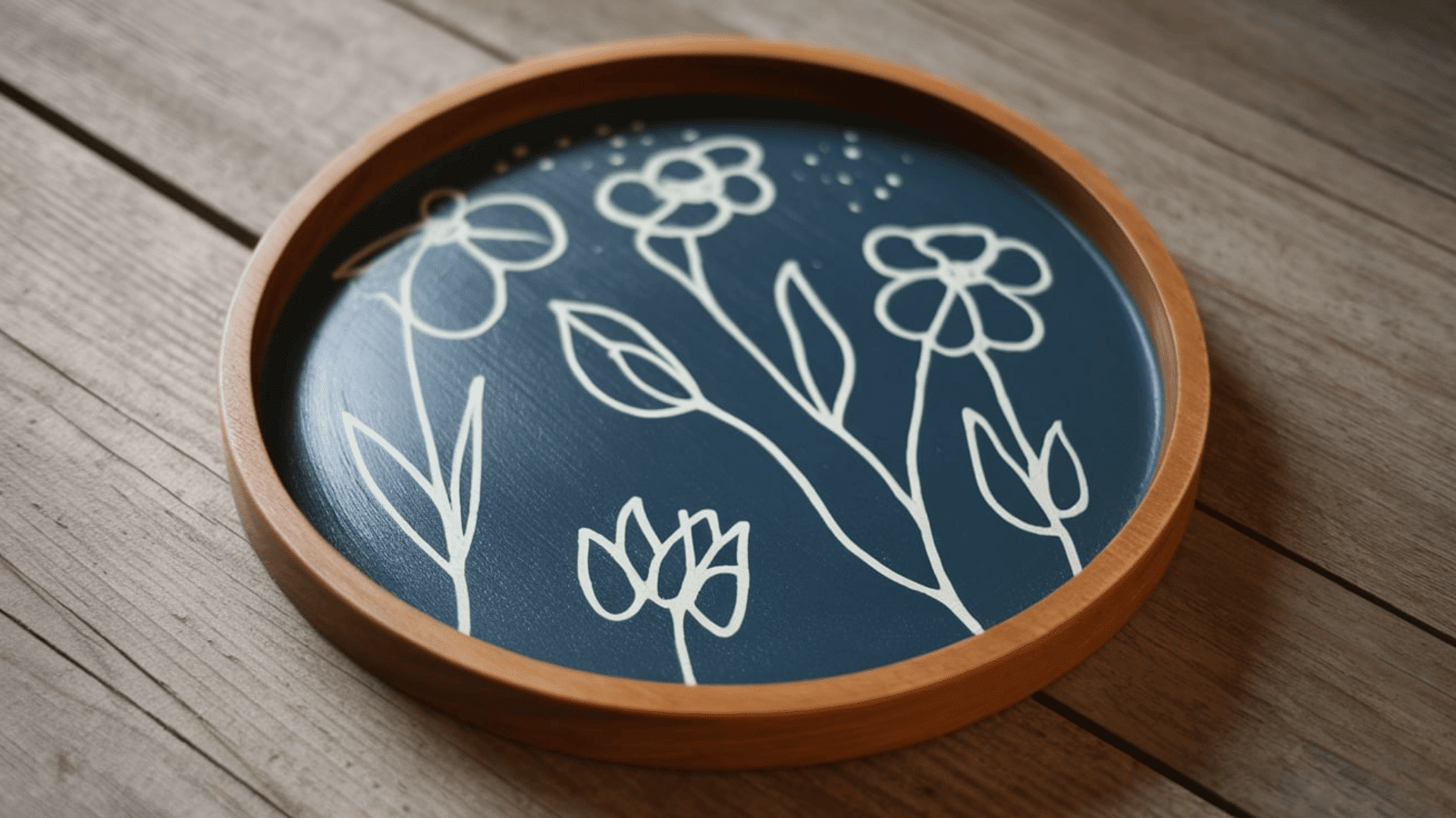 a round wooden tray painted navy blue with white hand drawn floral stem designs on a wooden surface