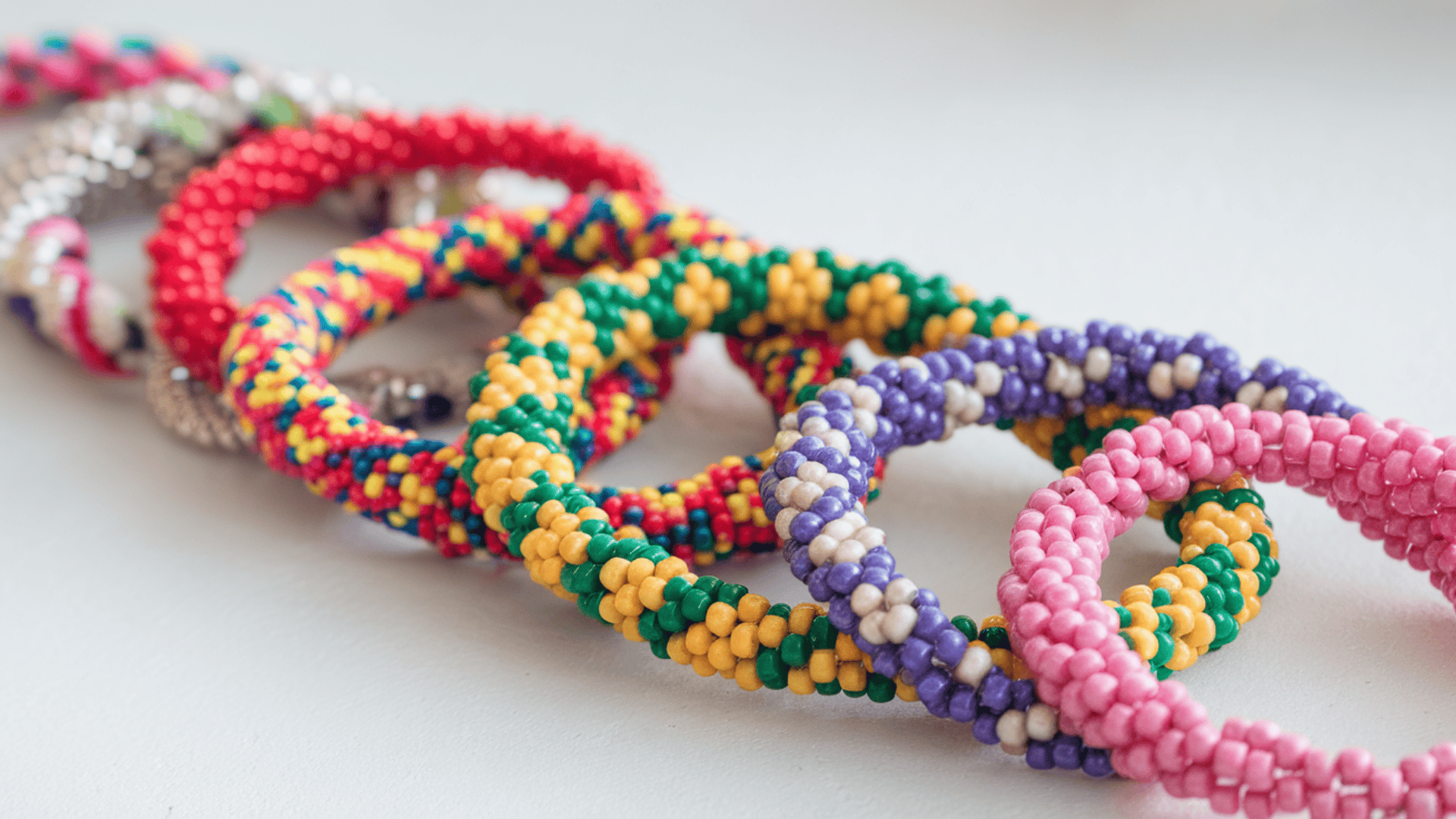 colorful handmade beaded bracelets in pink, yellow, green and purple patterns laid on a white surface