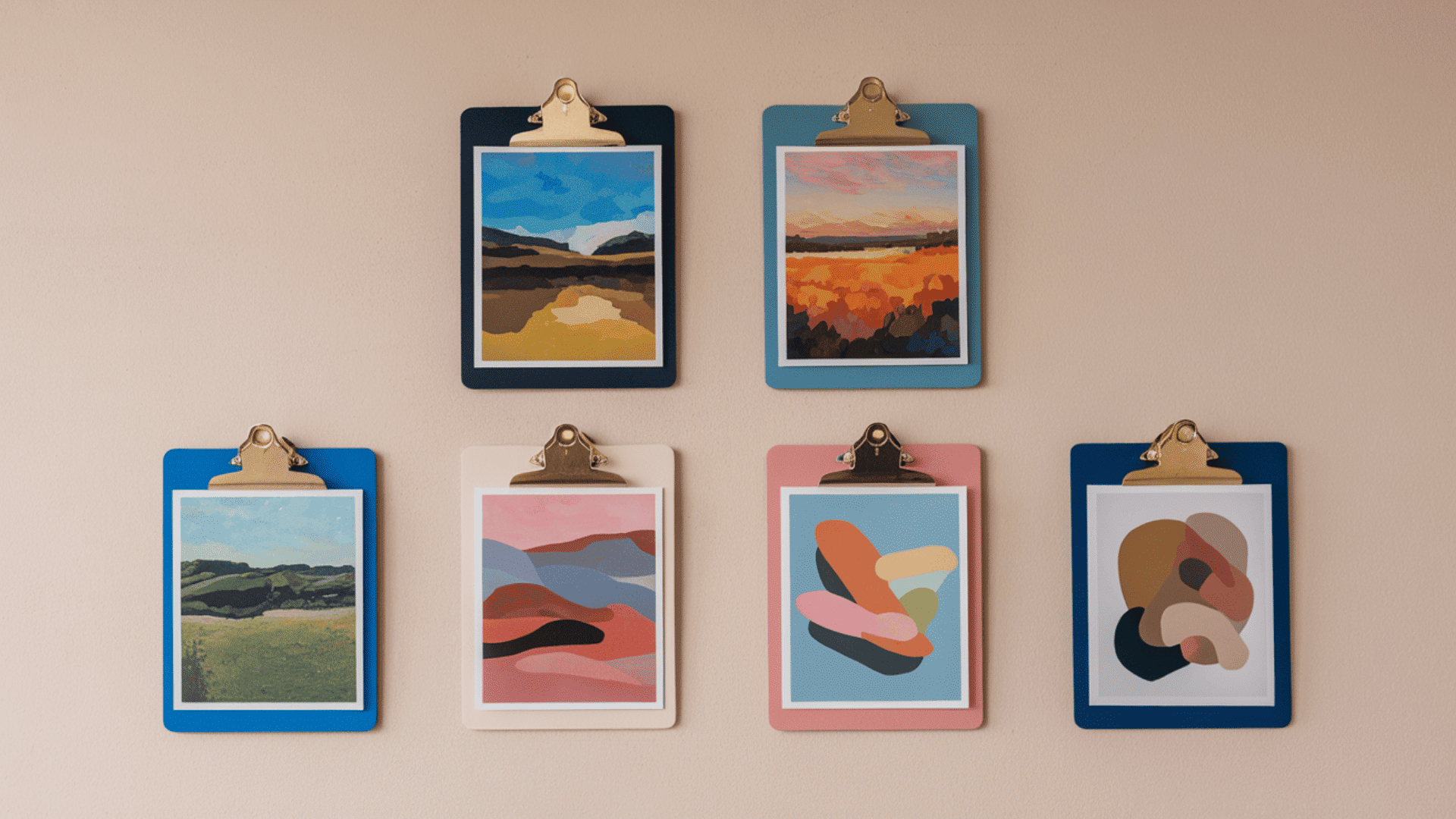 six colorful art prints clipped to painted clipboards in navy pink and blue hung on a beige wall