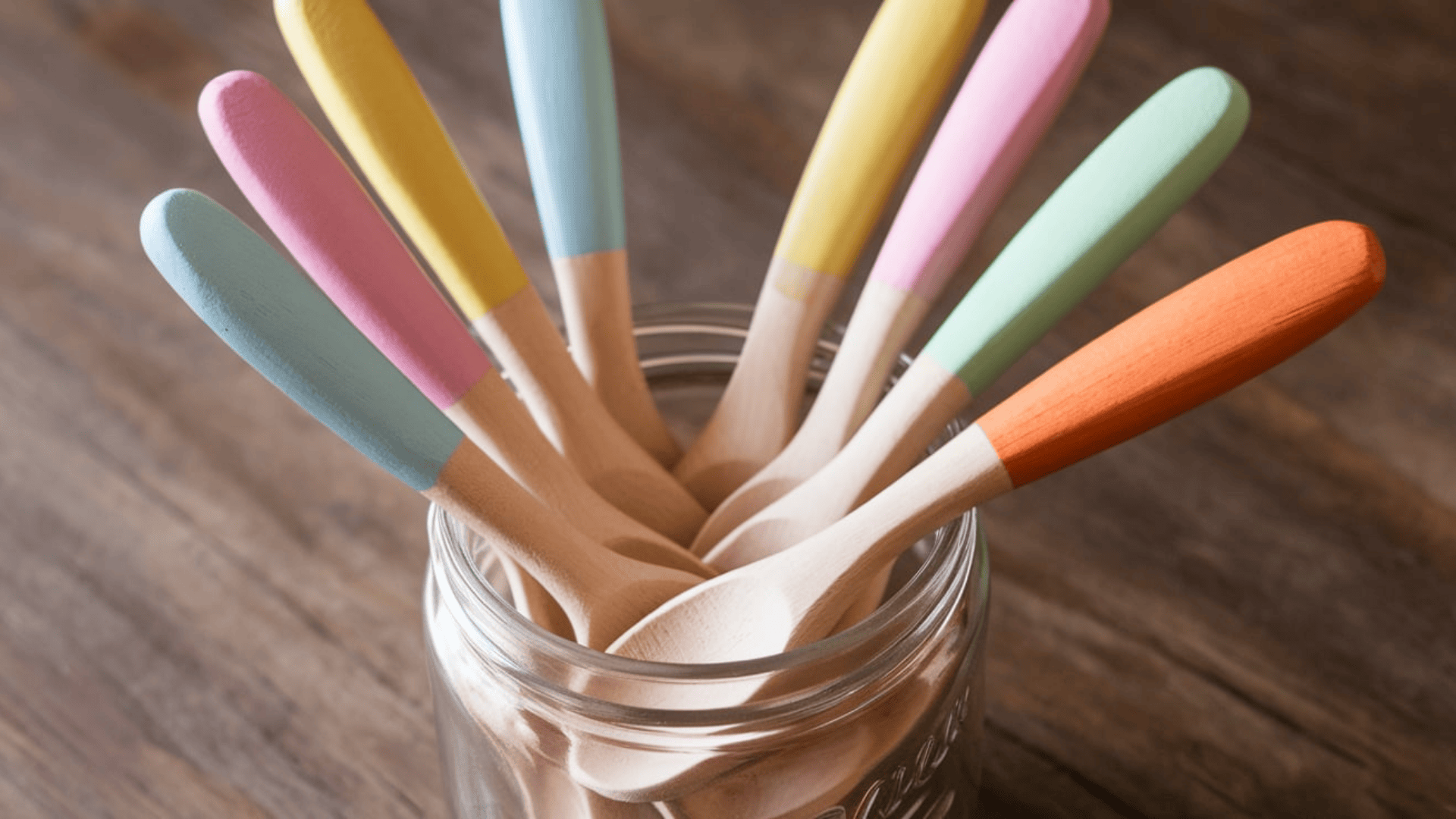 wooden spoons with pastel painted tips in blue, pink, yellow and orange stored in a glass mason jar